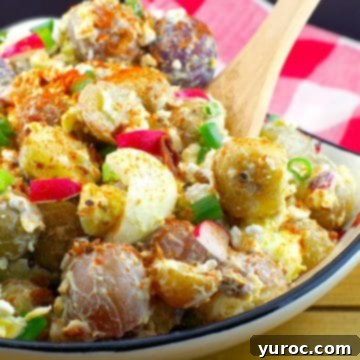 Pierogi Potato salad in a Ukrainian print dish with wooden spoon and checkered red and white towel in the background.