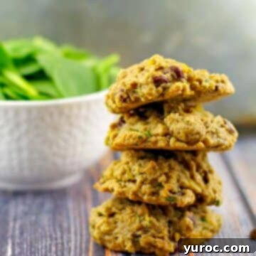 Four healthy chocolate spinach cookies stacked with a bowl of fresh spinach in the background.