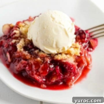 Rhubarb crumble in a white bowl, with a fork and ice cream on top.
