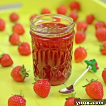 Strawberry jam in a jar with strawberries around it on a yellow surface.