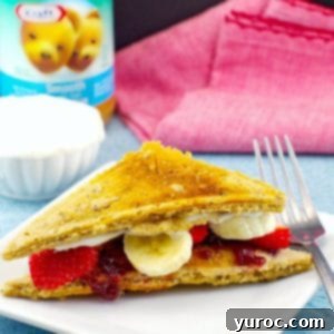 PB&J pancake sandwich on white plate with peanut butter, yogurt and red napkin in the background
